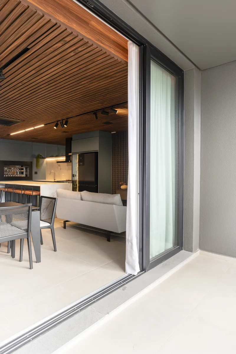 Porta de correr aberta ligando a sala ao terraço, com perfil branco e vidro do piso ao teto