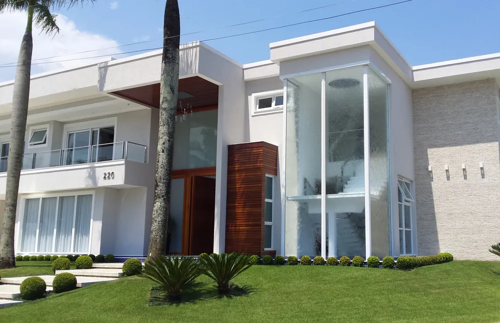 Residência contemporânea de dois pavimentos com grandes panos de vidro e esquadrias brancas